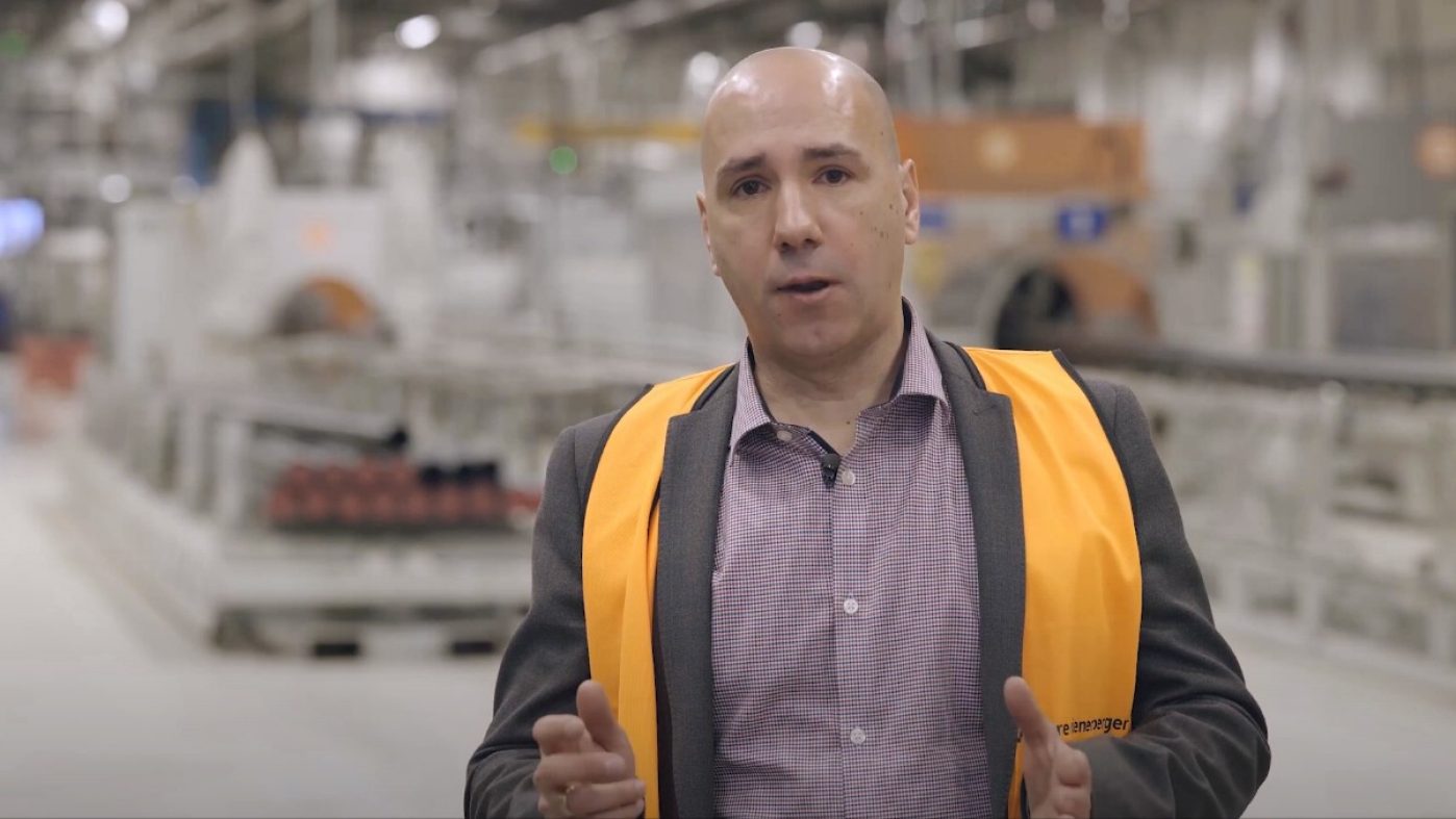 man with bald head and safety west in a production hall, talking