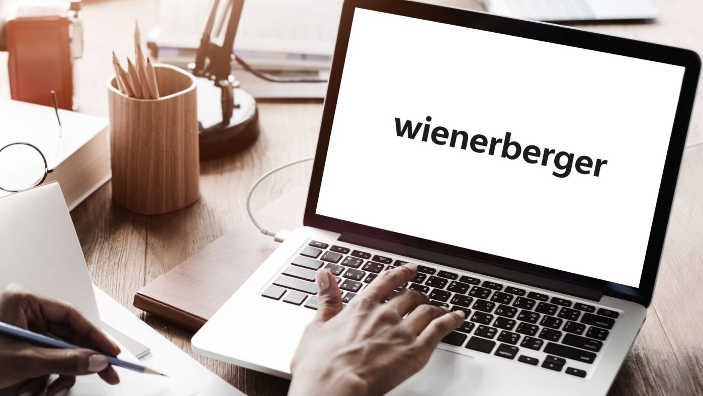 Someone typing on a laptop, pencil and notebook, Wienerberger logo on the screen